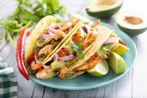 Mexican tacos with shrimpguacamole and vegetables on wooden table