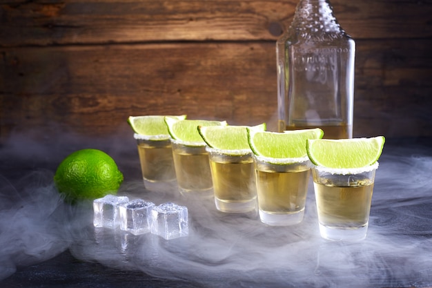 Mexican tequila gold in short glasses with salt, lime slices and ice on a wooden table. smoke.