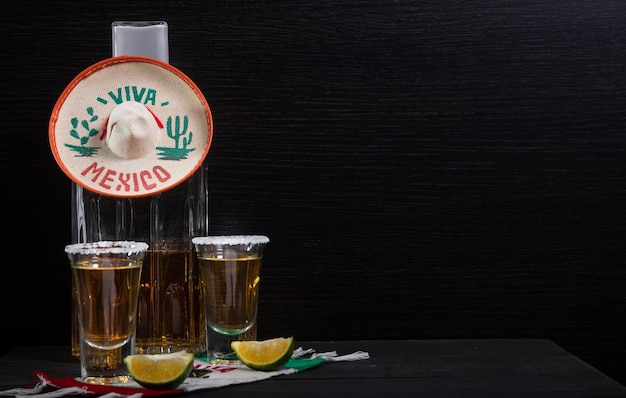 Mexican tequila shots accompanied by a luxury square bottle on a wooden table with lemons