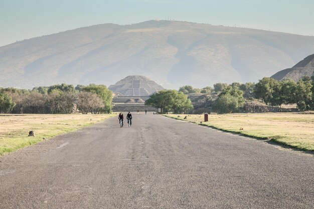 メキシコシティメキシコ2012年3月2日テオティワカンメキシコの背景に太陽のピラミッドと死者のepmtyアベニューで早朝に自転車に乗るカップル