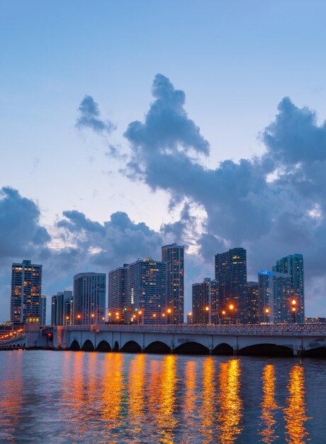 Miami, Florida cityscape skyline on Biscayne Bay. Panorama at dusk with urban skyscrapers and bridge over sea with reflection.