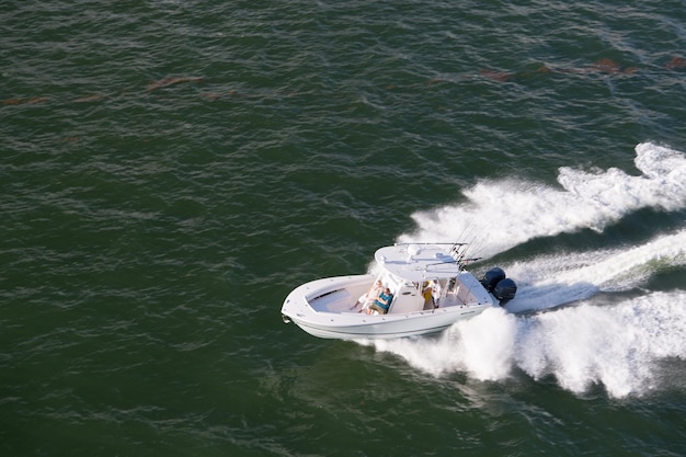 Майами, США - 17 декабря 2015: белая современная моторная лодка с людьми едет на скорости по синему морю или поверхности океана с волнами на красивом морском пейзаже