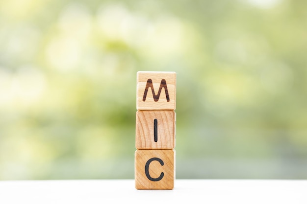 MIC word is written on wooden cubes on a green summer background Closeup of wooden elements