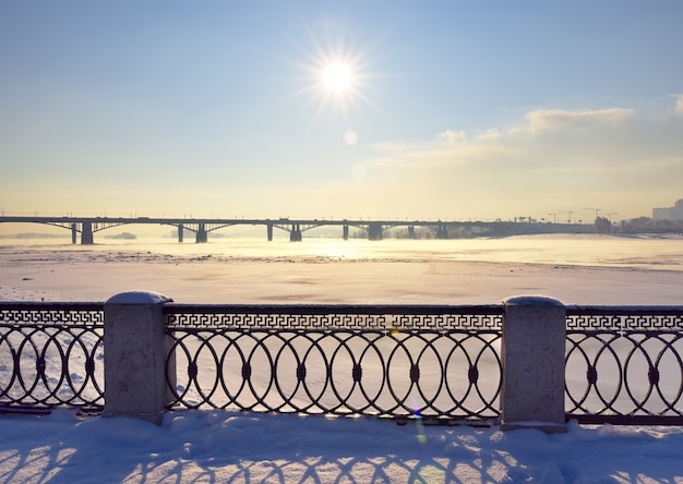 Michael's waterfront in winter. Metal fence of the Ob river Bank, Oktyabrsky bridge in the distance