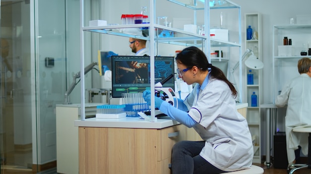 顕微鏡下でサンプルを見ている現代の実験室で新しいワクチンのために働いている微生物学者。科学研究のためのハイテクおよび化学ツールを使用してウイルスの進化を調査する多民族チーム。
