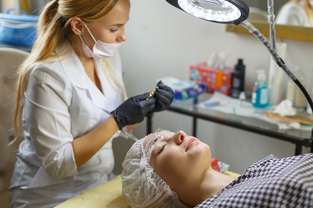 Photo microblading eyebrows work flow in a beauty salon. woman having her eye brows tinted. semi-permanent makeup for eyebrows. focus on model's face and eyebrow