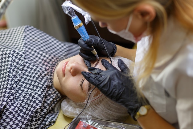 Microblading wenkbrauwen werkstroom in een schoonheidssalon. Vrouw die haar wenkbrauwen heeft getint. Semi-permanente make-up voor wenkbrauwen. Focus op het gezicht en de wenkbrauw van het model