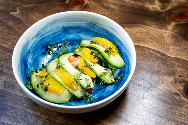 Микрозелень на авокадо, креветках и апельсиновом салате в синей тарелке. Стол сервировочный для фото и видеосъемки.