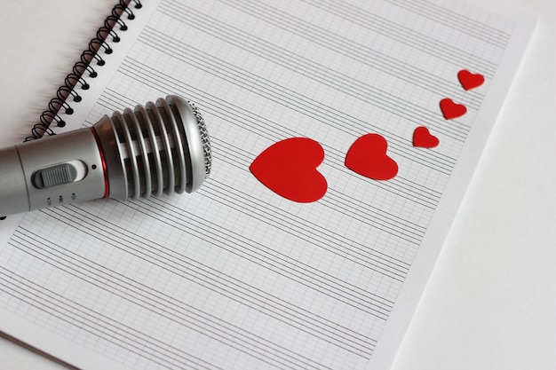 Microfono e cuori rossi di carta si trovano su un notebook musicale pulito. il concetto di musica e amore.