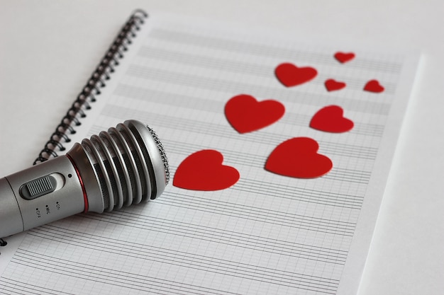 Microphone and paper red hearts are located on a clean music notebook. 