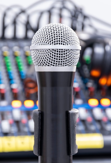 The microphone on tripod in the center of the image with mixer background in sound control room