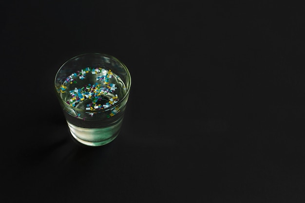 Microplastic in glass of water on black background