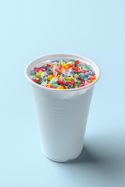 水を入れた白いプラスチックカップのマイクロプラスティック パステルブルーの背景 マイクロプラスティックの問題概念