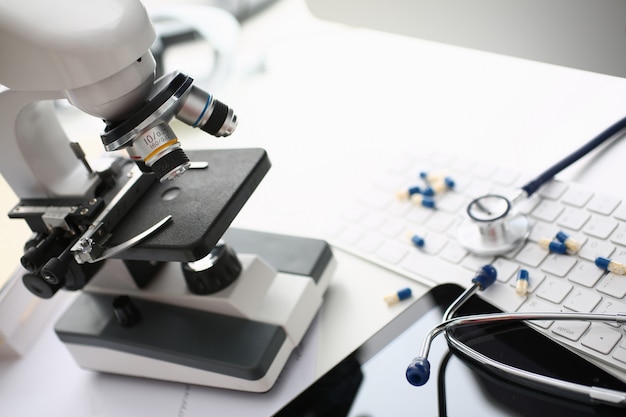 Microscope, stethoscope and pills on white keyboard