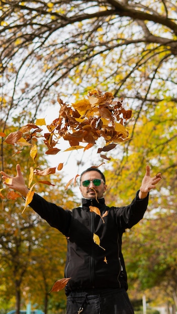 Mid 30\'s man with glasses and dark clothes in the forest\
throwing leaves giving an effect of magic and weightlessness\
connection with nature in the fall and winter season copy space\
vertical shot