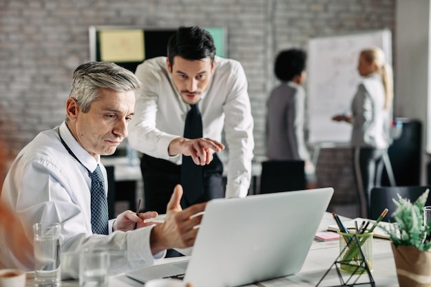 Mid adult businessman consulting with his younger colleague about email he received while working in the office