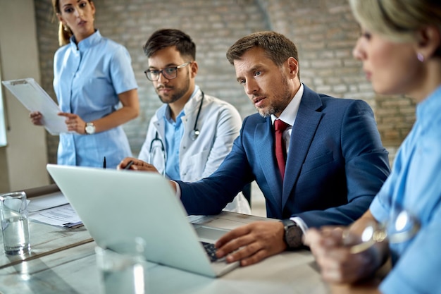 Mid adult businessman and healthcare workers cooperating while working on a computer during a meeting in the office