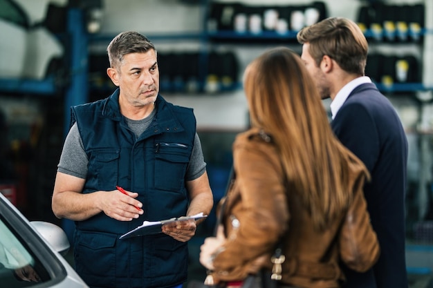 Mid adult car repairman communicating with a couple at auto repair workshop