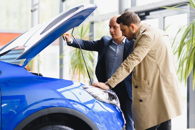 Metà venditore di auto per adulti che mostra il motore al cliente presso la concessionaria