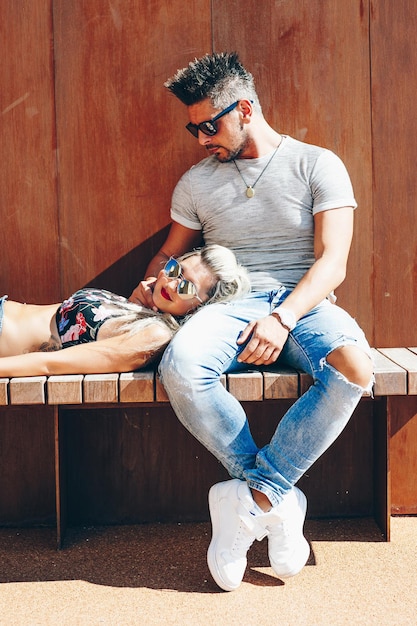 Mid adult couple sitting on boardwalk against wooden wall during sunny day