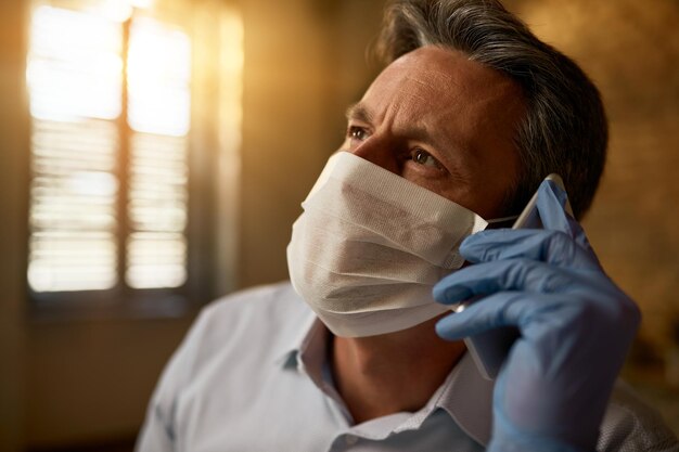 Mid adult entrepreneur wearing face mask while communicating\
over mobile phone in the office during covid19 pandemic