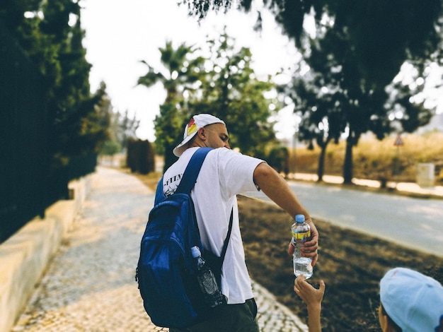 Foto uomo adulto medio che dà una bottiglia d'acqua a suo figlio sul marciapiede