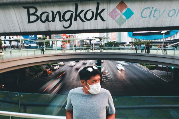 Foto uomo adulto medio che indossa una maschera antinfluenza mentre si trova su un ponte pedonale sulla strada in città