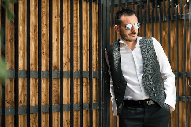 Photo mid adult man wearing sunglasses while standing wooden gate