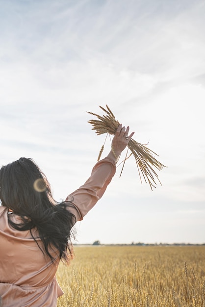 Metà donna adulta in camicia beige in piedi su un campo di grano con alba sullo sfondo vista posteriore