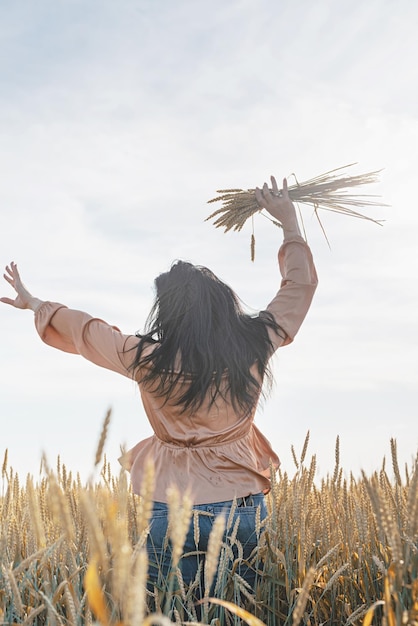 Mid adult woman in beige shirt standing on a wheat field with
sunrise on the background back view