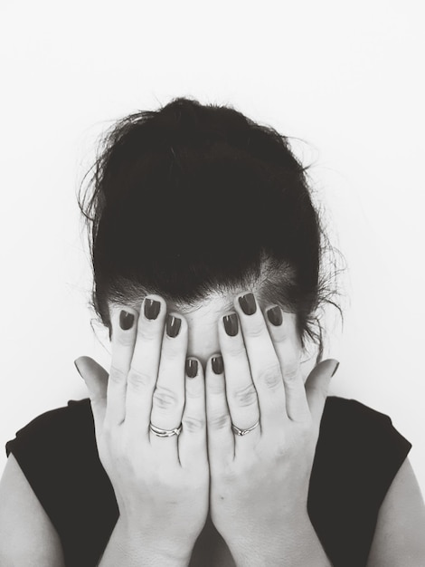 Mid adult woman covering face with hands against white background