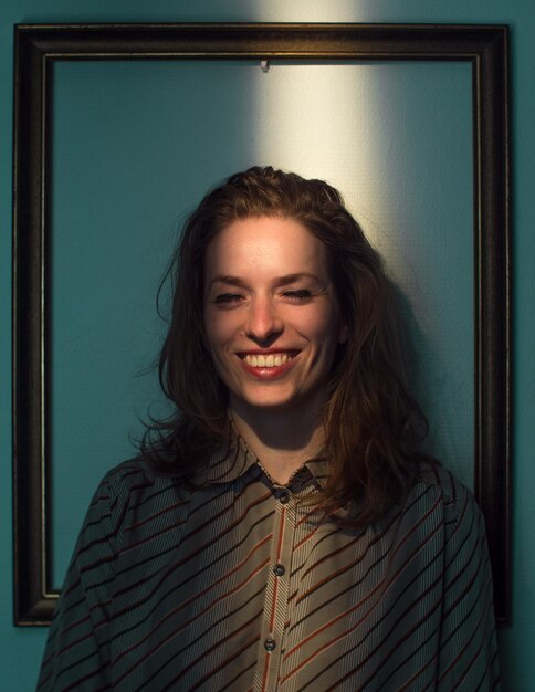 Photo mid adult woman standing against picture frame on wall