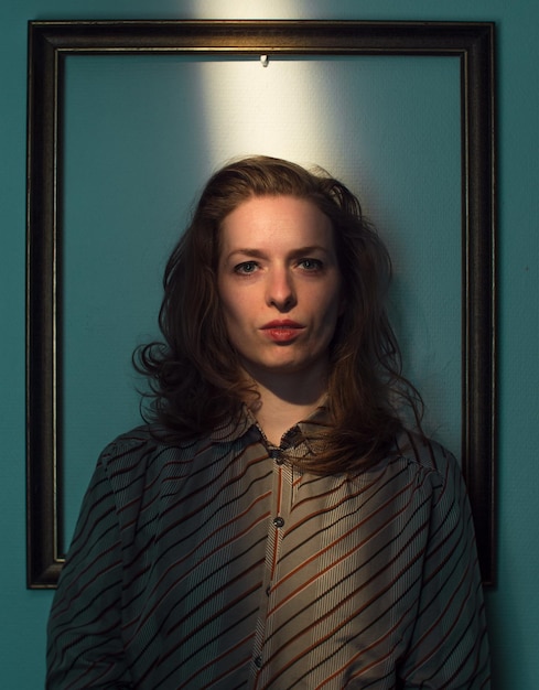 Photo mid adult woman standing against picture frame on wall