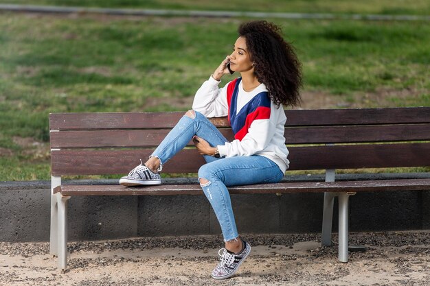 mid adult woman talking through smart phone while sitting on bench at park