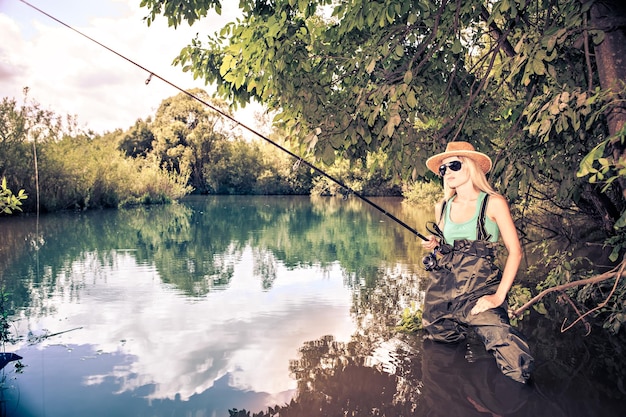 Foto donna adulta a metà che indossa occhiali da sole che pesca in piedi nel lago