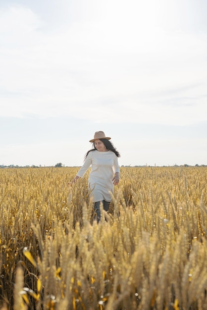 Женщина среднего возраста в белом платье стоит на пшеничном поле с восходом солнца на заднем плане
