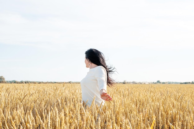 Mid adult woman in white dress standing on a wheat field with
sunrise on the background back view