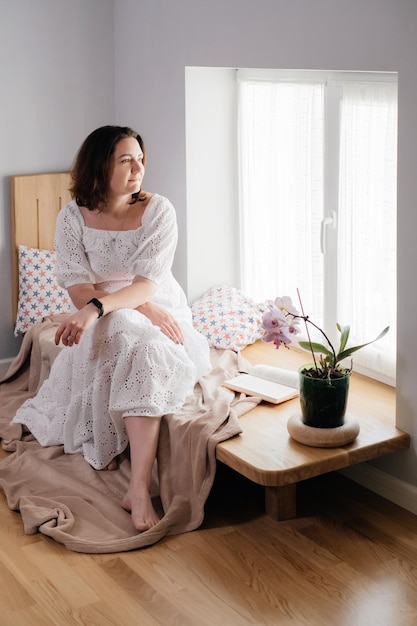 Mid age adult woman plus size reading a book by the window