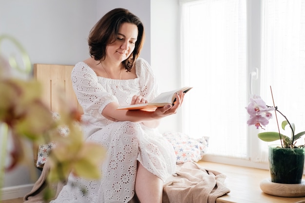 Donna adulta di mezza età che legge un libro vicino alla finestra