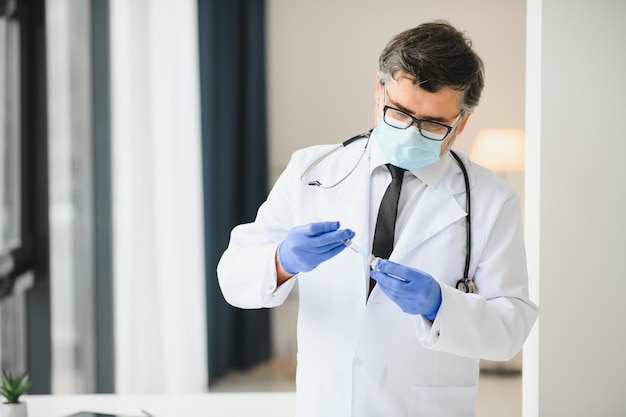 Photo mid aged male doctor wearing protective mask holding a syringe with vaccine