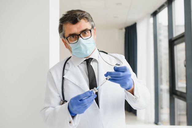 Mid aged male doctor wearing protective mask holding a syringe with vaccine