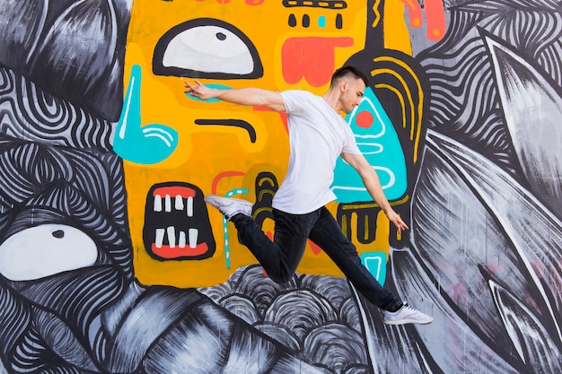 Photo mid-air shot of handsome man against graffiti wall