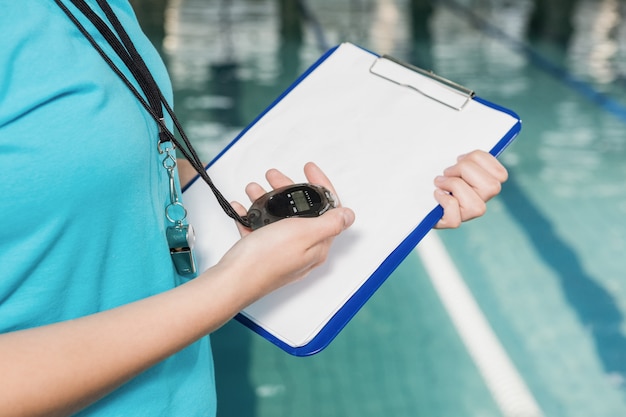 Mid sectie van coach met een stopwatch en klembord bij zwembad