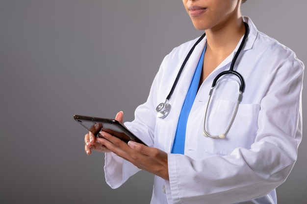 Mid section of african american female doctor using digital tablet against grey background