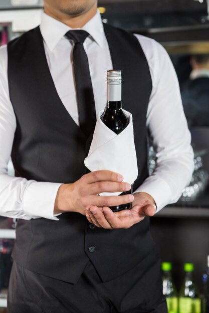 Mid section of bartender holding a wine bottle in bar