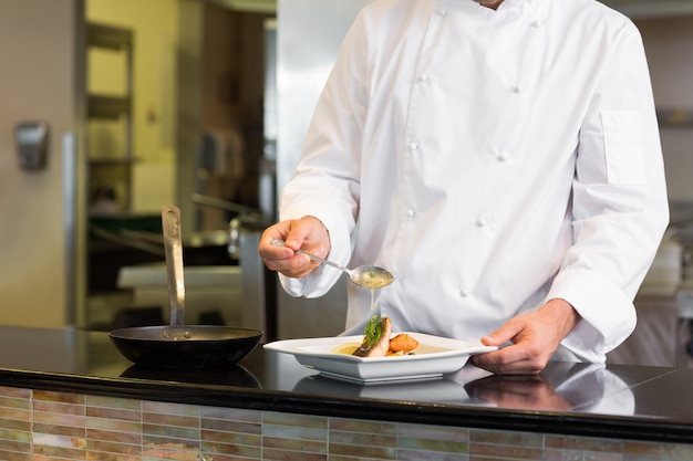 Mid section of a chef garnishing food in kitchen