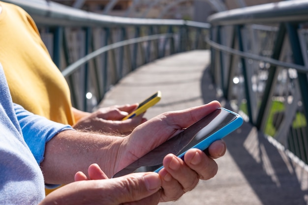 Mid section of a couple of people holding cell phone in hand, covers matched with clothing. standing on a bridge over the city traffic