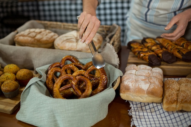 Mid section of female staff holding croissant with tong at counter