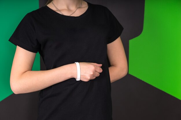 Mid section front view of young female wearing black t-shirt and white wristband, hand in a fist against abdomen, other hand behind back on a green and black background