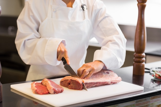 Metà di sezione delle mani che tagliano carne in cucina